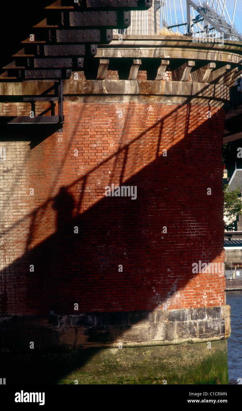 Ziegel-Pier von Hungerford Bridge, London, mit Schatten der Person zu Fuß über die Fußgängerbrücke Stockfoto
