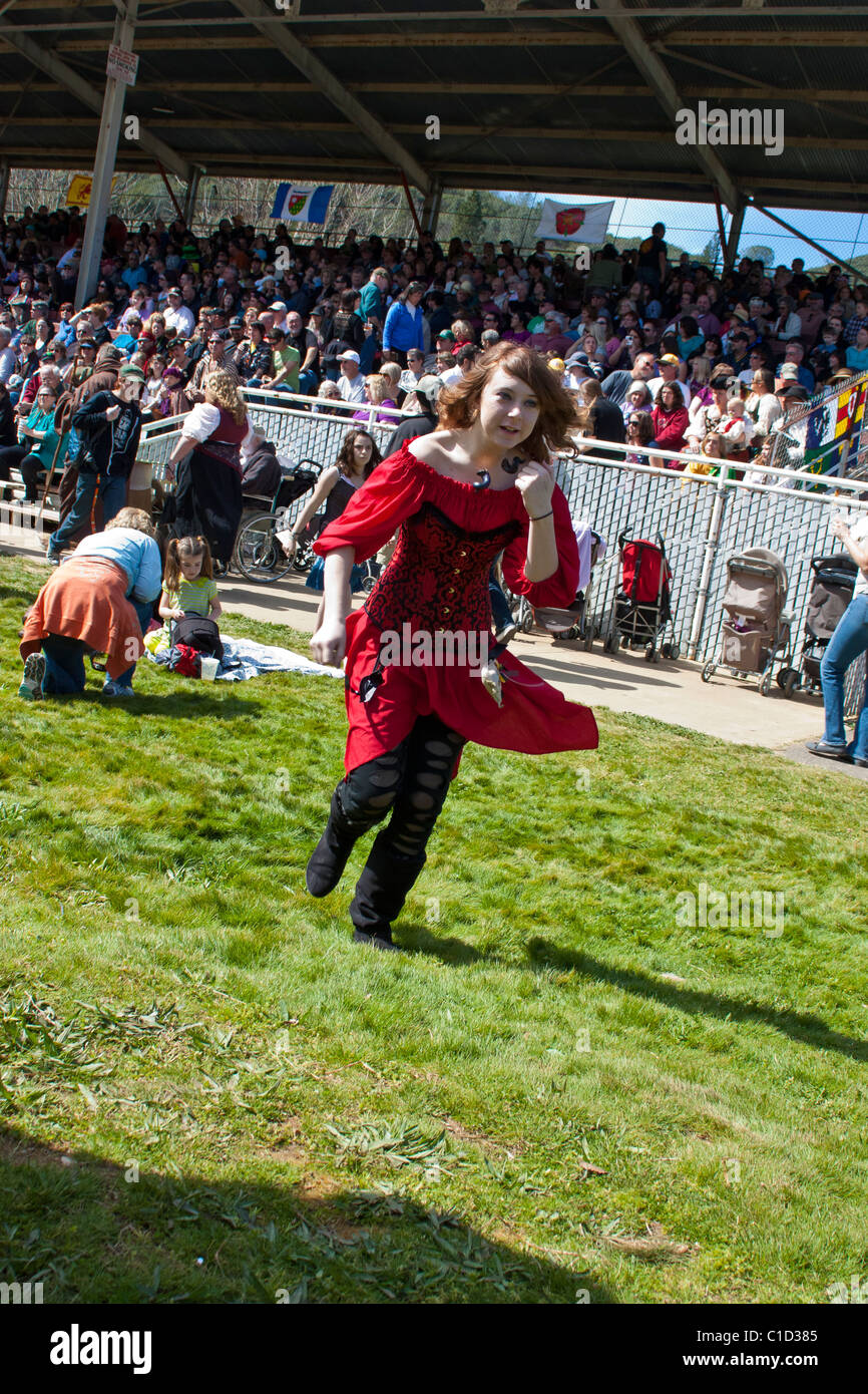 Ein rothaariges Mädchen, das sich in Kostümen für die Sonora California Celtic faire verkleidet hat, mit der Menge, die hinter ihr das Jousting-Spiel beobachtet Stockfoto