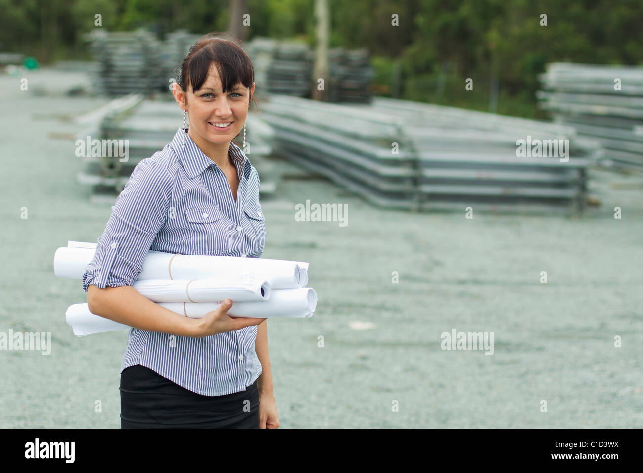 Junger Ingenieur Frau betreuenden Hof mit gerollten Zeichnungen in ihrer hand Stockfoto