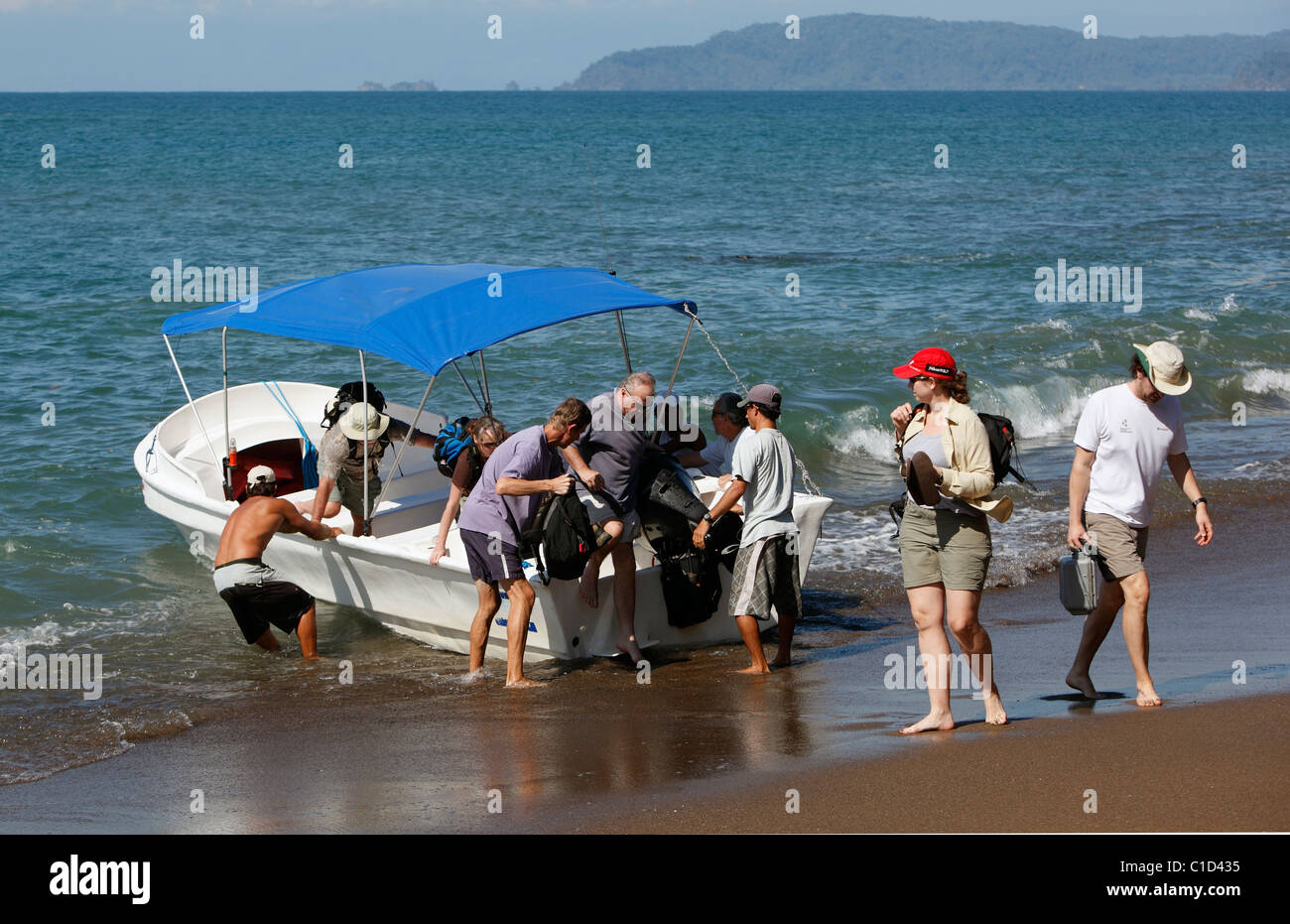 Touristen gehen am Strand von einem kleinen touristischen Boot, Drake Bay, Halbinsel Osa, Costa Rica Stockfoto