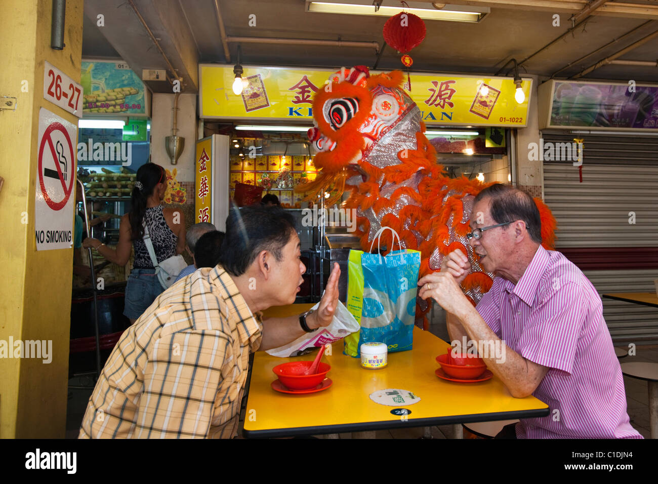Männer Essen in einem Hawker centre mit Löwen Tanz Performern im Hintergrund.  Chinatown, Singapur Stockfoto