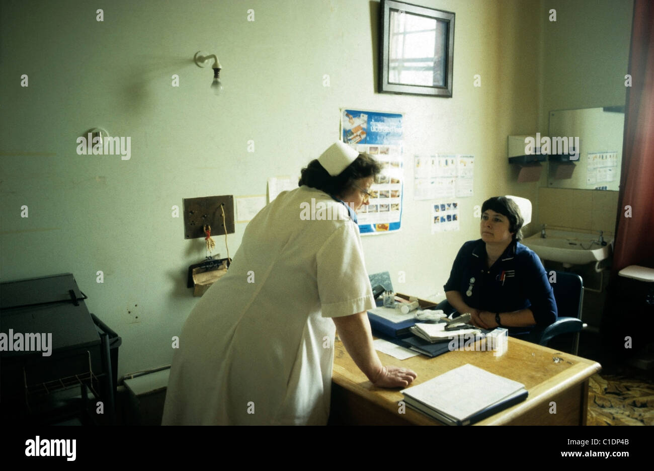 Eine Krankenschwester des NHS in weißer Uniform, die mit einer Krankenschwester in blauer Uniform spricht, die an einem Verwaltungstisch im Büro des Bronglais-Krankenhauses in Ceredigion West Wales sitzt Großbritannien 1970er, 1980er Jahre, 1983 KATHY DEWITT Stockfoto