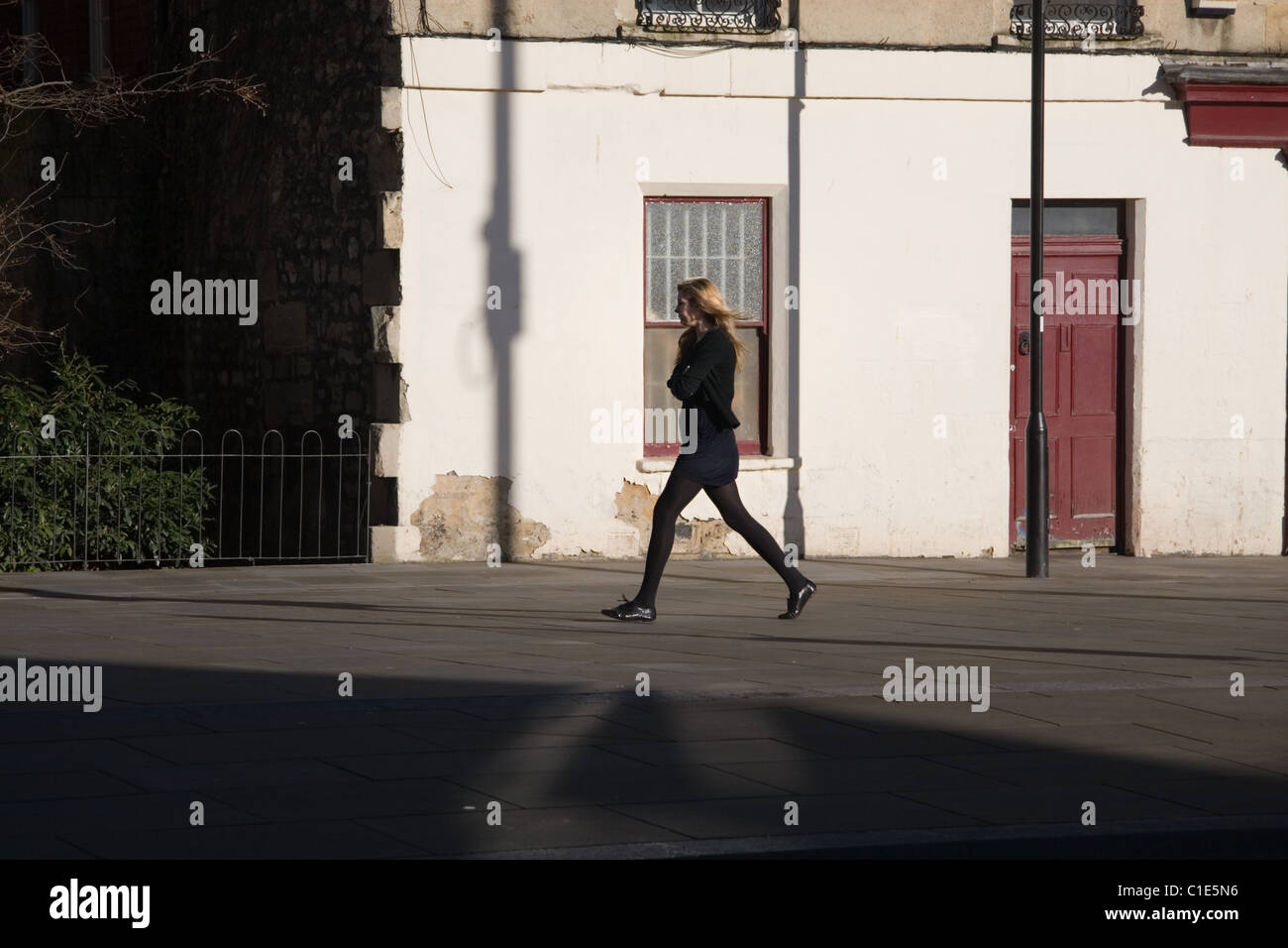 Eine junge Frau, die zügig entlang einer Stadtstraße im Sonnenlicht Stockfoto