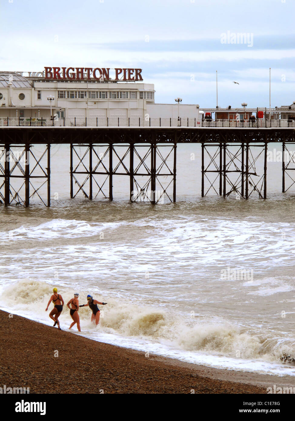 Drei Schwimmer trotzen die kalten Winter-Wellen der Englisch-Kanäle mit Brighton Pier im Hintergrund. Stockfoto