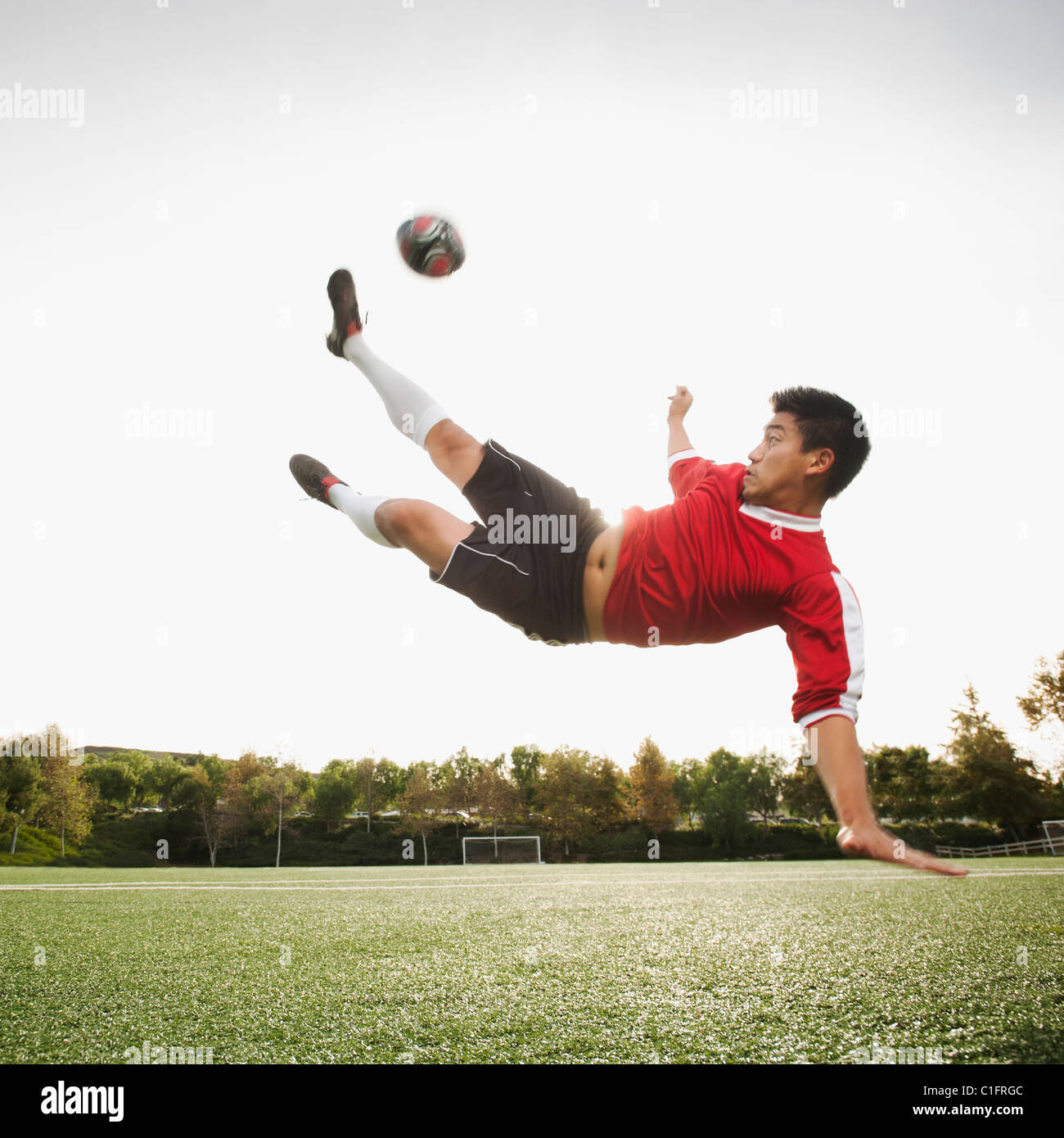 Asiatische Fußball-Spieler in der Luft treten Fußball Stockfoto