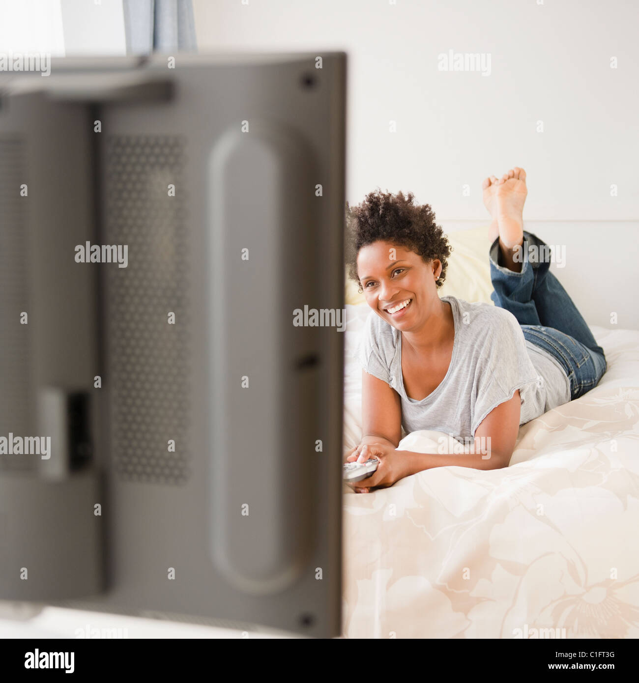 Schwarze Frau auf Bett vor dem Fernseher Stockfoto