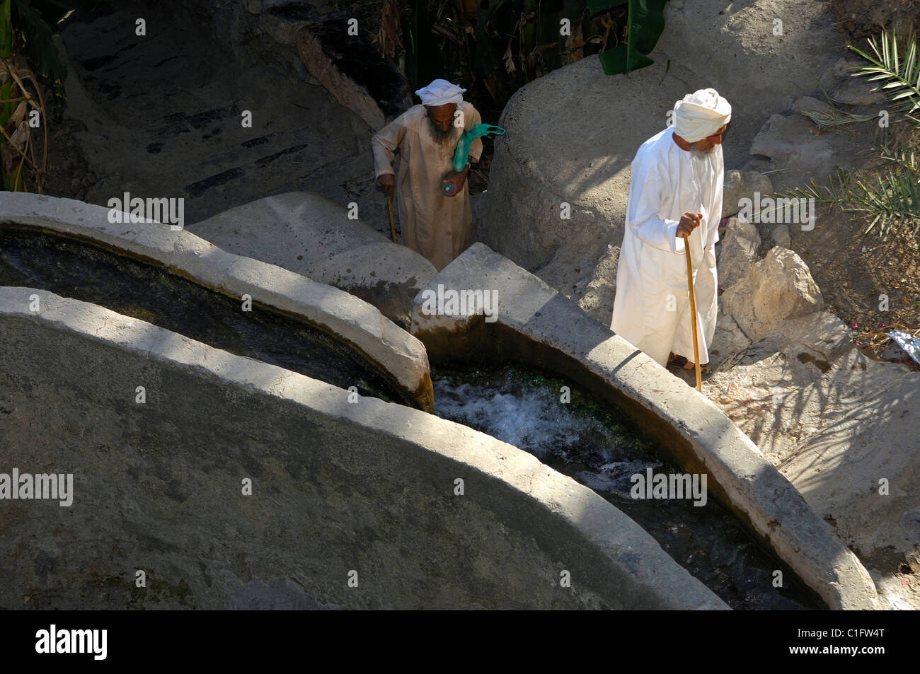 Elder omanischen Männer in traditioneller Kleidung vorbeigehen eine Bewässerung-Kanal, Misfah al-Ibriyeen, Sultanat von Oman Stockfoto