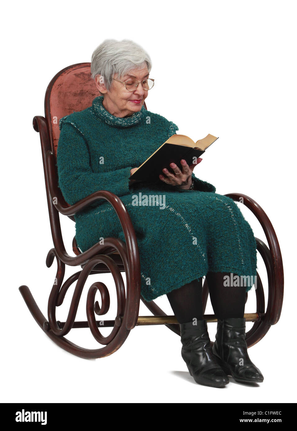 Alte Frau liest ein schwarzes Buch während der Sitzung in einer Wippe, isoliert auf einem weißen Hintergrund. Stockfoto