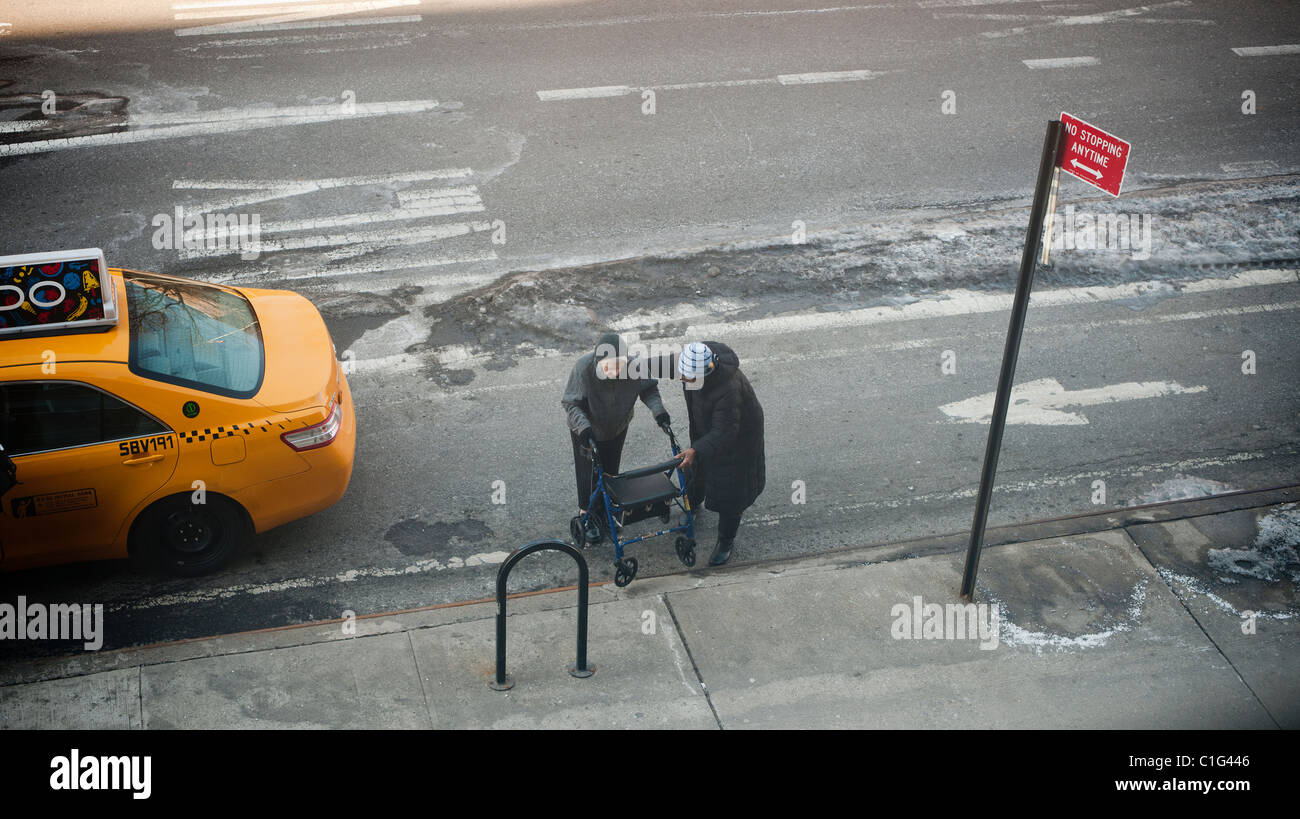 Eine ältere Frau wird von ihrem Berater im New Yorker Stadtteil Chelsea an den Straßenrand unterstützt. Stockfoto
