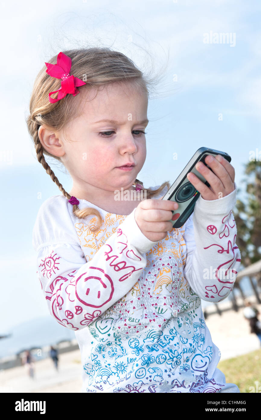 Ein kleines dreijähriges Mädchen spielt mit einer Hand gehalten elektronisches Spiel. Stockfoto