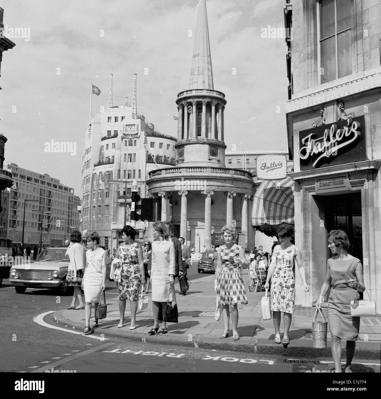 1960er Jahre, Frauen, die auf einem Bürgersteig stehen und kurz davor sind, eine Straße in der Regent Street, London, hinter der All Souls Church und dem Broadcasting House, Heimstadion der BBC, zu überqueren. Stockfoto
