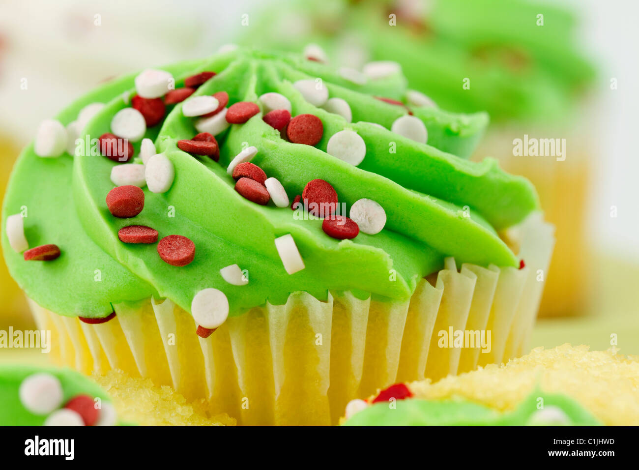 Nahaufnahme von Vanille Cupcake mit grünen Zuckerguss und rote und weiße Streusel mit defokussierten Hintergrund. Stockfoto