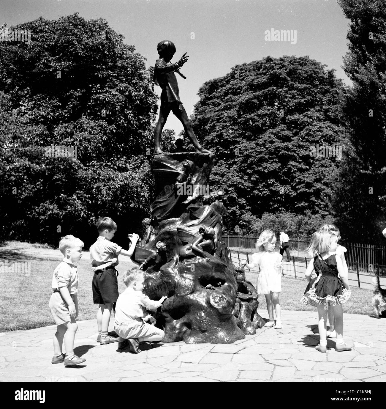 1950er Jahre, Sommer und kleine Kinder spielen an der Bronzestatue von Peter Pan in Kensington Gardens, London, eine Figur von J. M. Barrie. Stockfoto