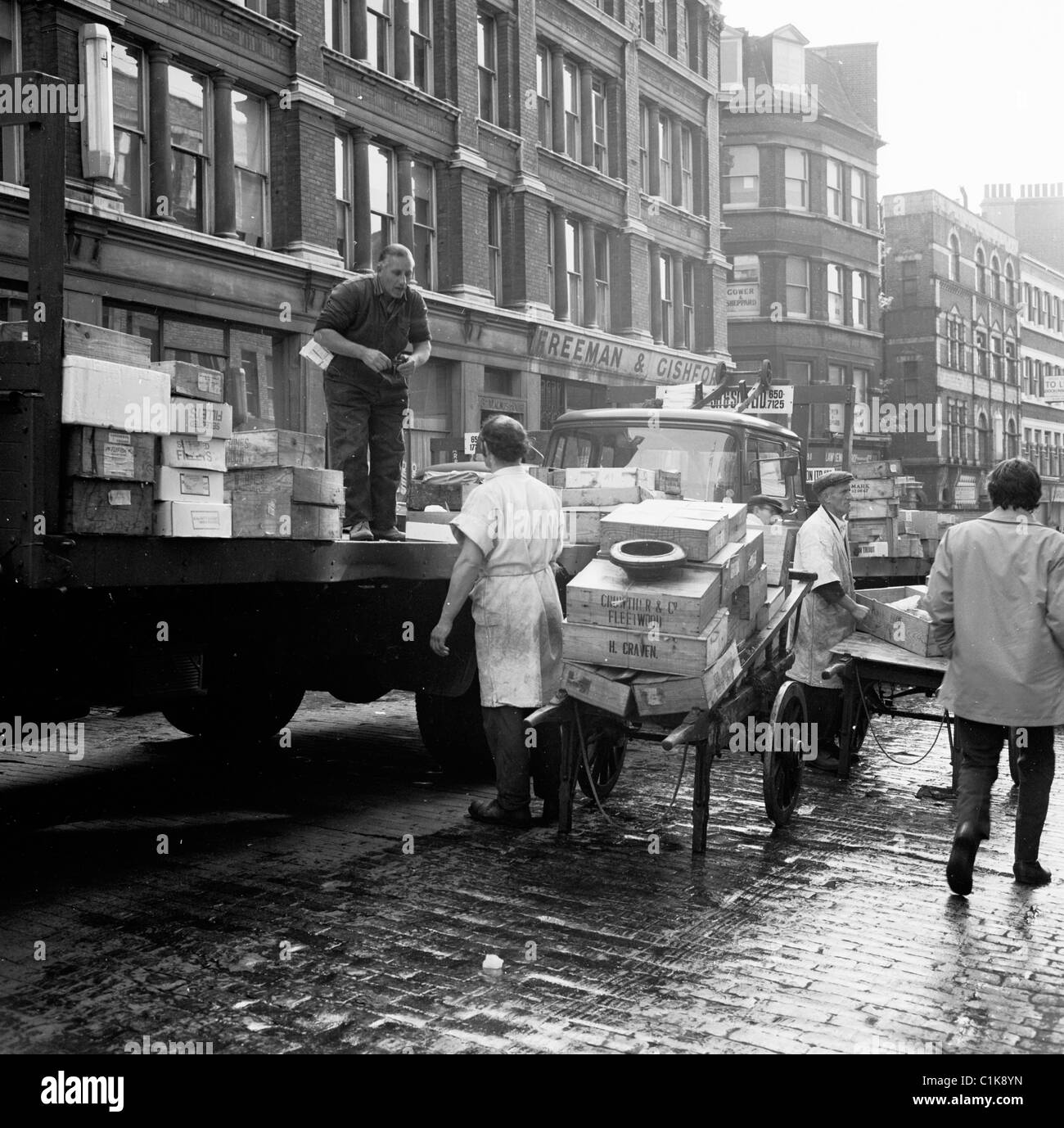 Auf einer nassen Kopfsteinpflasterstraße aus den 1950er Jahren laden Träger Fische von einem LKW auf Karren auf dem berühmten Billingsgate Fish Market in der Lower Thames Street, London. Stockfoto