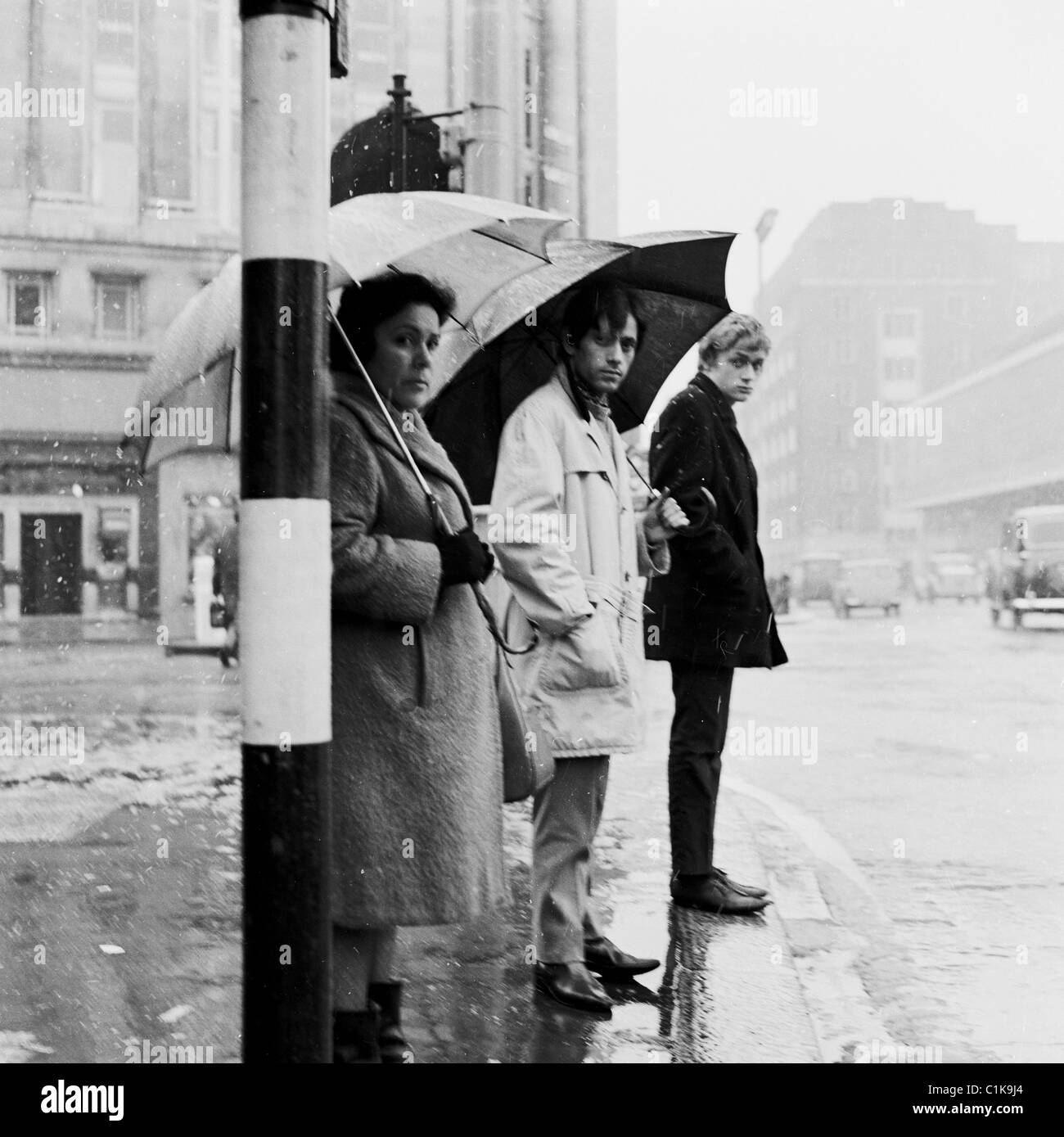 der 1950er Jahre. winter Zeit und -Schirme, wie Menschen in Regen und Kälte in London an einer Bushaltestelle in dieses Bild von J Allan Cash warten. Stockfoto