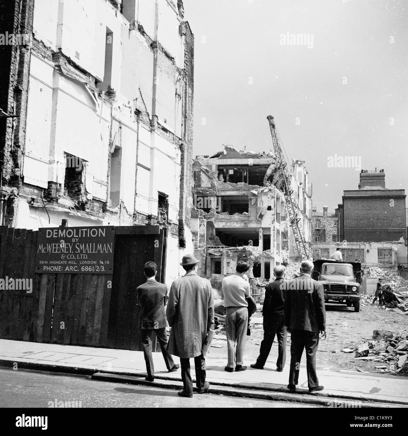 1950er Jahre London. Gruppe der Männer stehen auf einem Bürgersteig gerade ein Abriss eines Gebäudes in diesem historischen Bild statt. Stockfoto