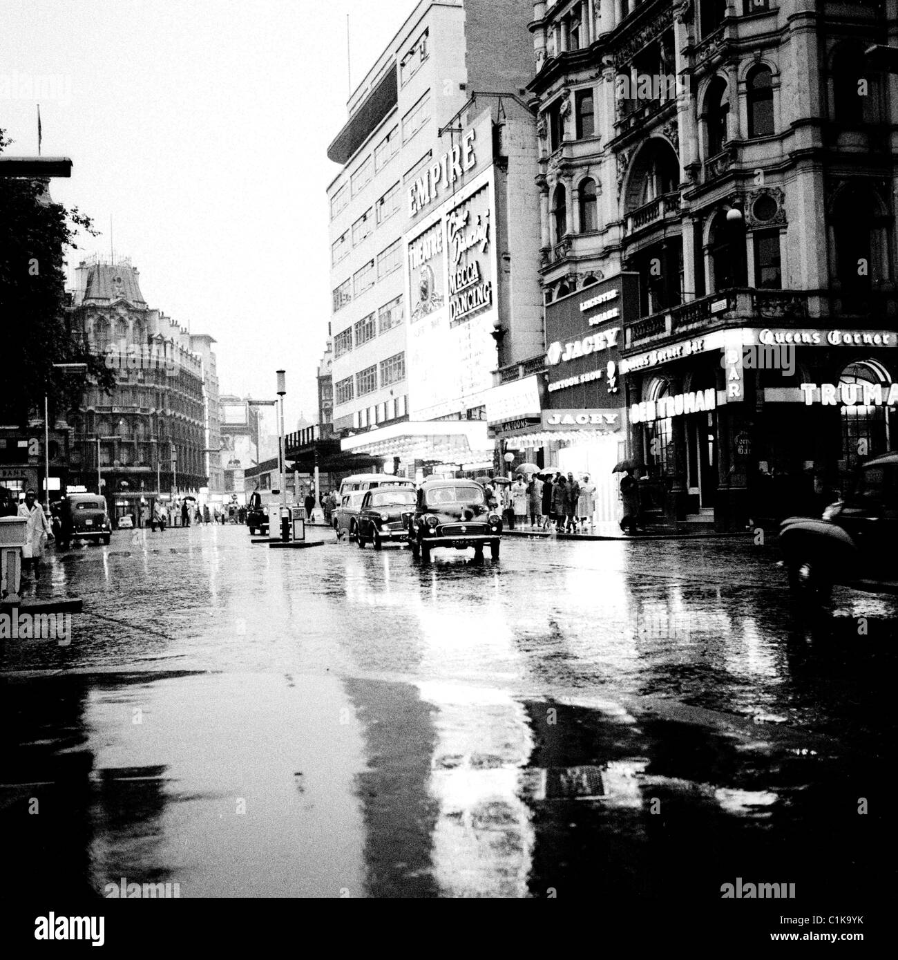 1960er Jahre London. Autos bewegen sich langsam auf den Regen durchnässt Straße außerhalb der Empire-Kino im West End in diesem historischen Bild. Stockfoto