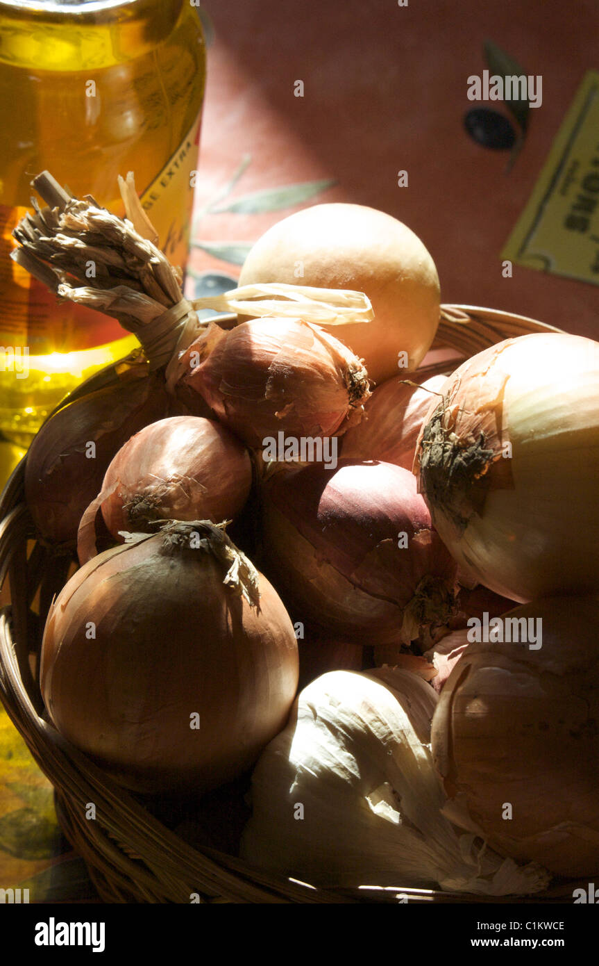 Gelbe Zwiebeln und Schalotten in einem Weidenkorb mit Olivenöl aus der Provence im Sommerlicht einer Küche in der Provence Stockfoto