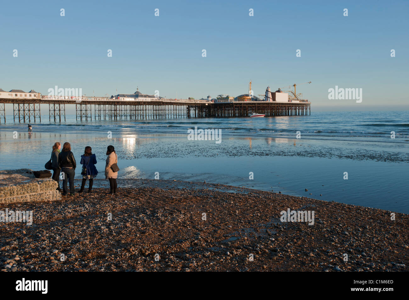Vier Frauen Palace Pier von Brighton bei Ebbe im frühen Frühlingssonnenschein betrachten. Brighton, East Sussex, England, UK. Stockfoto