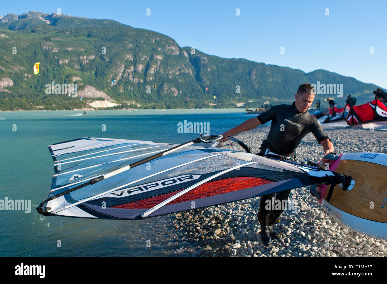 Ein Windsurfer trägt sein Board aus dem Wasser am Ende des Tages. Stockfoto