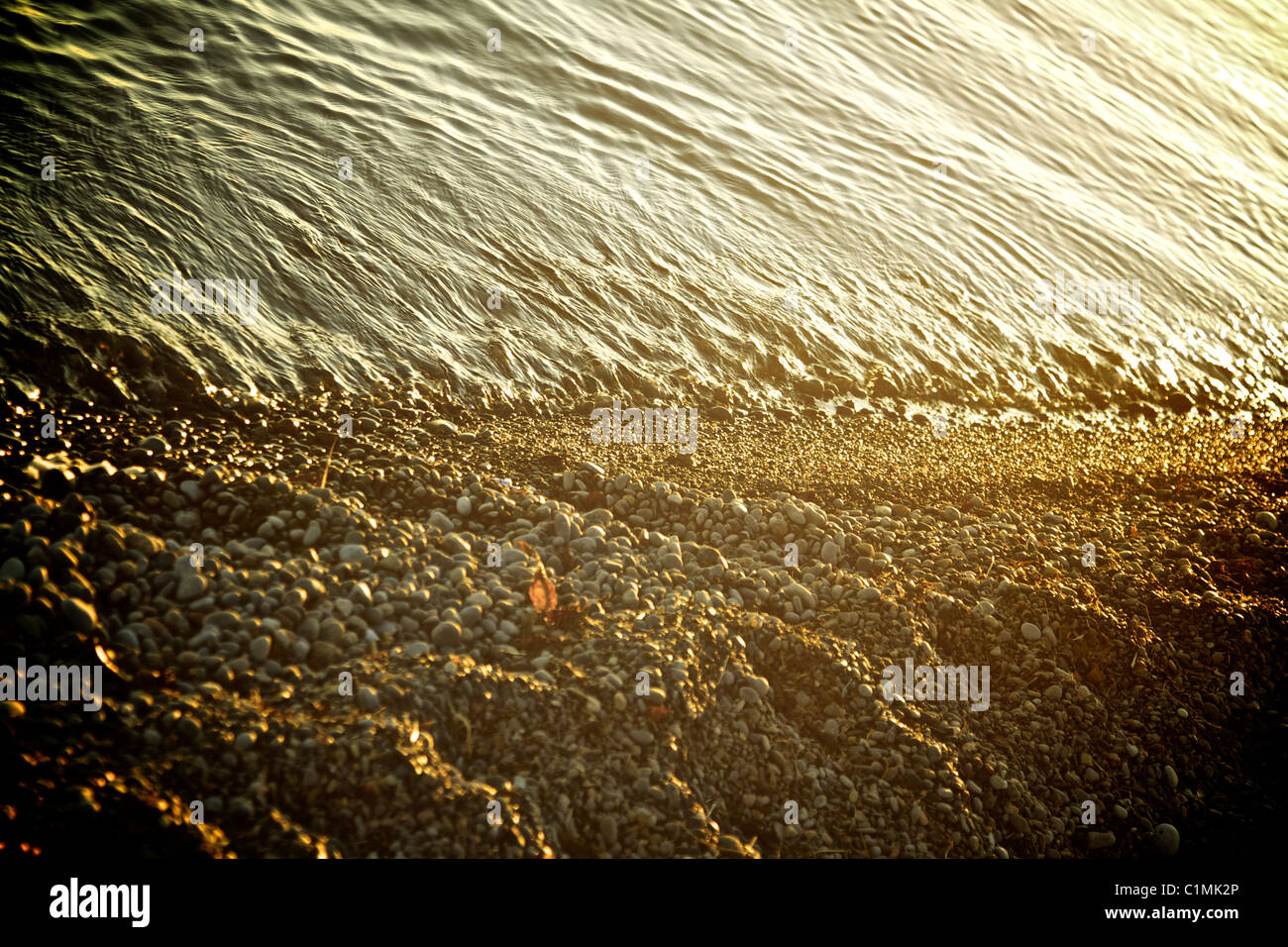 Uferlinie mit Wasser und Steinen, tiefstehende Sonne und Farbe optimiert. Stockfoto