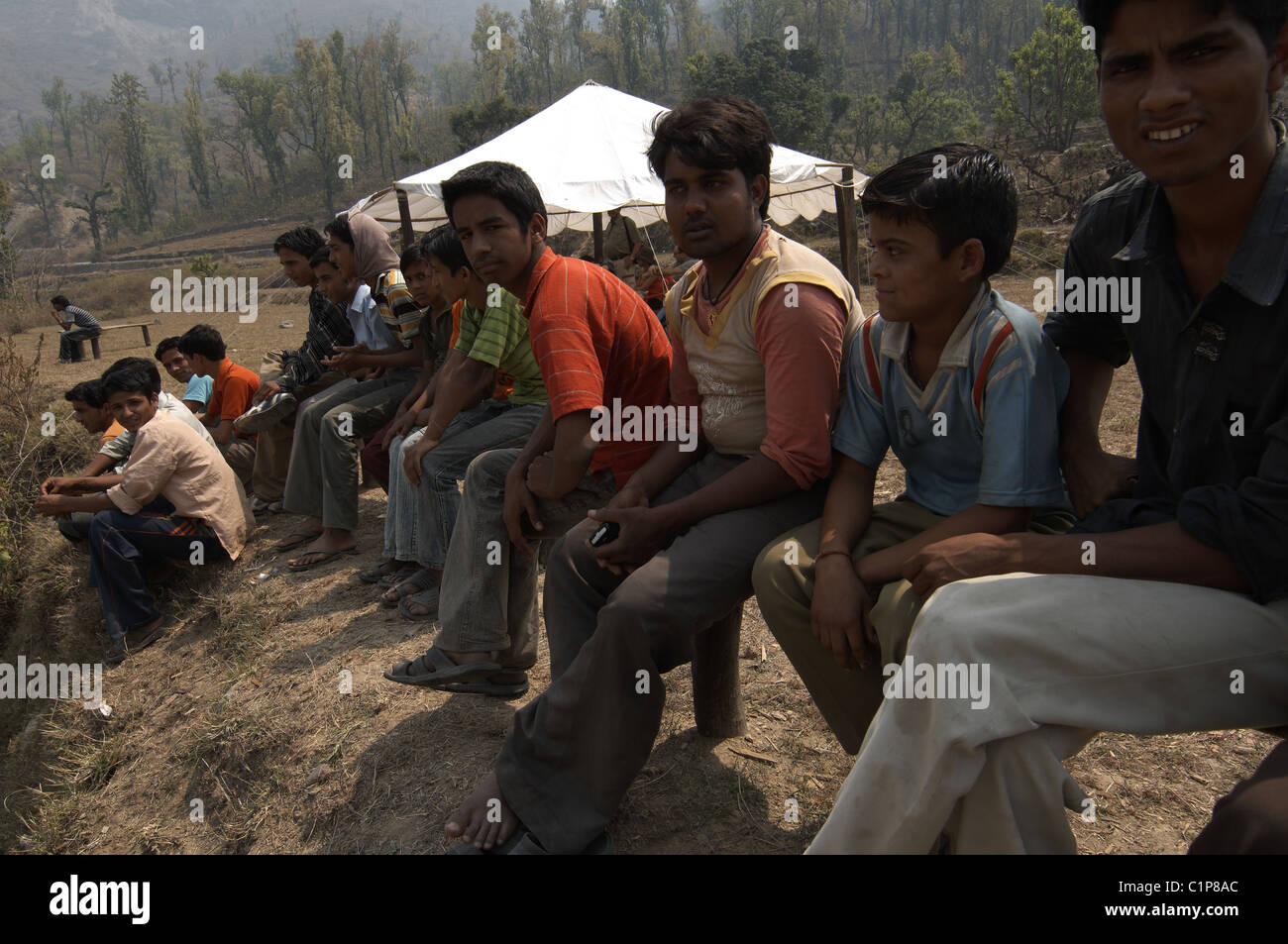 Eine Gruppe von Männern sitzen und beobachten ein Cricket match auf einem Feld im Jim Corbett Nationalpark in Indien. Stockfoto