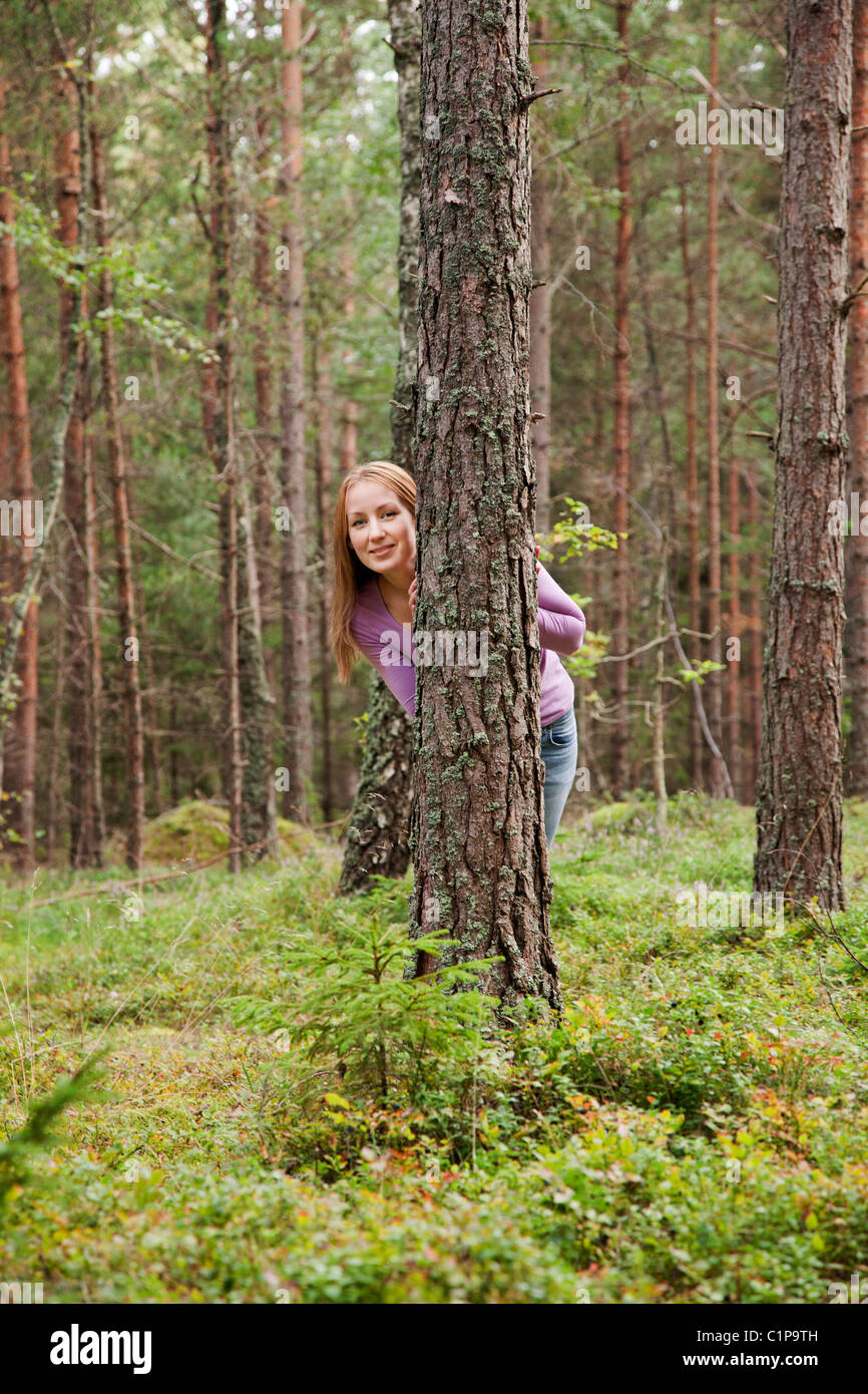 Junge Frau versteckt sich hinter einem Baum im Wald Stockfoto