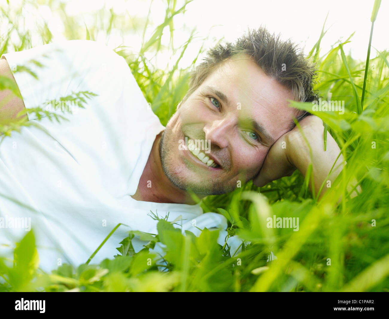 Ekero, junger Mann auf dem Rasen liegen, wegsehen und lächelnd Stockfoto