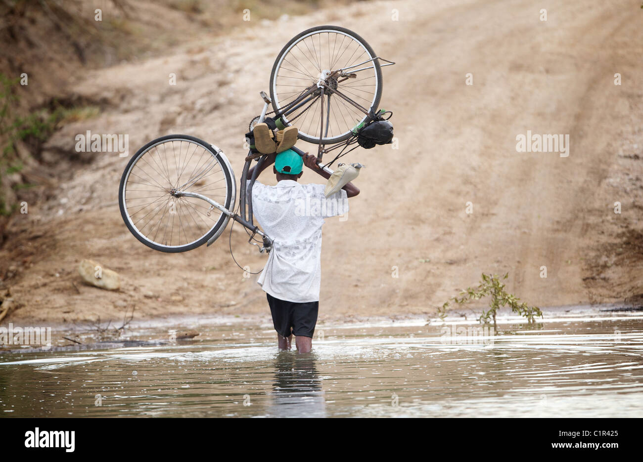 Mann trägt Fahrrad durch Fluss in Saadani Tansania Afrika Stockfoto