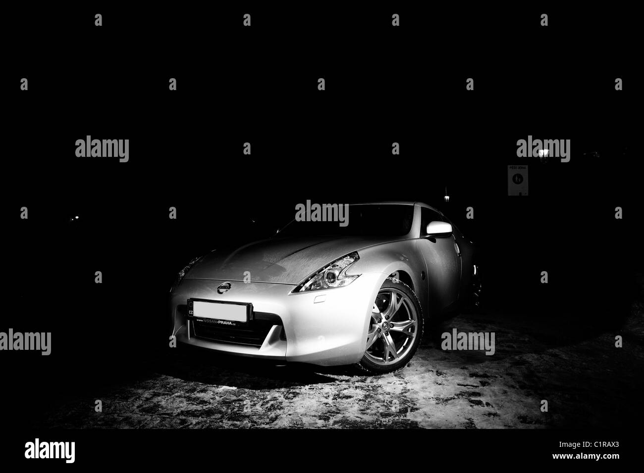 Die monochromatischen Farbtöne eines eleganten Sportwagens, die in einer nächtlichen Umgebung erfasst werden und dessen Konturen von einem einsamen Licht beleuchtet werden Stockfoto