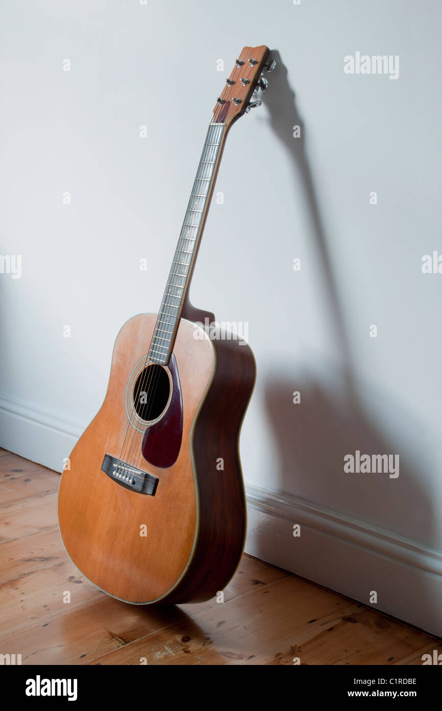 6-saitige Akustikgitarre (Yamaha), die sich gegen eine weiße Wand lehnt. Stockfoto