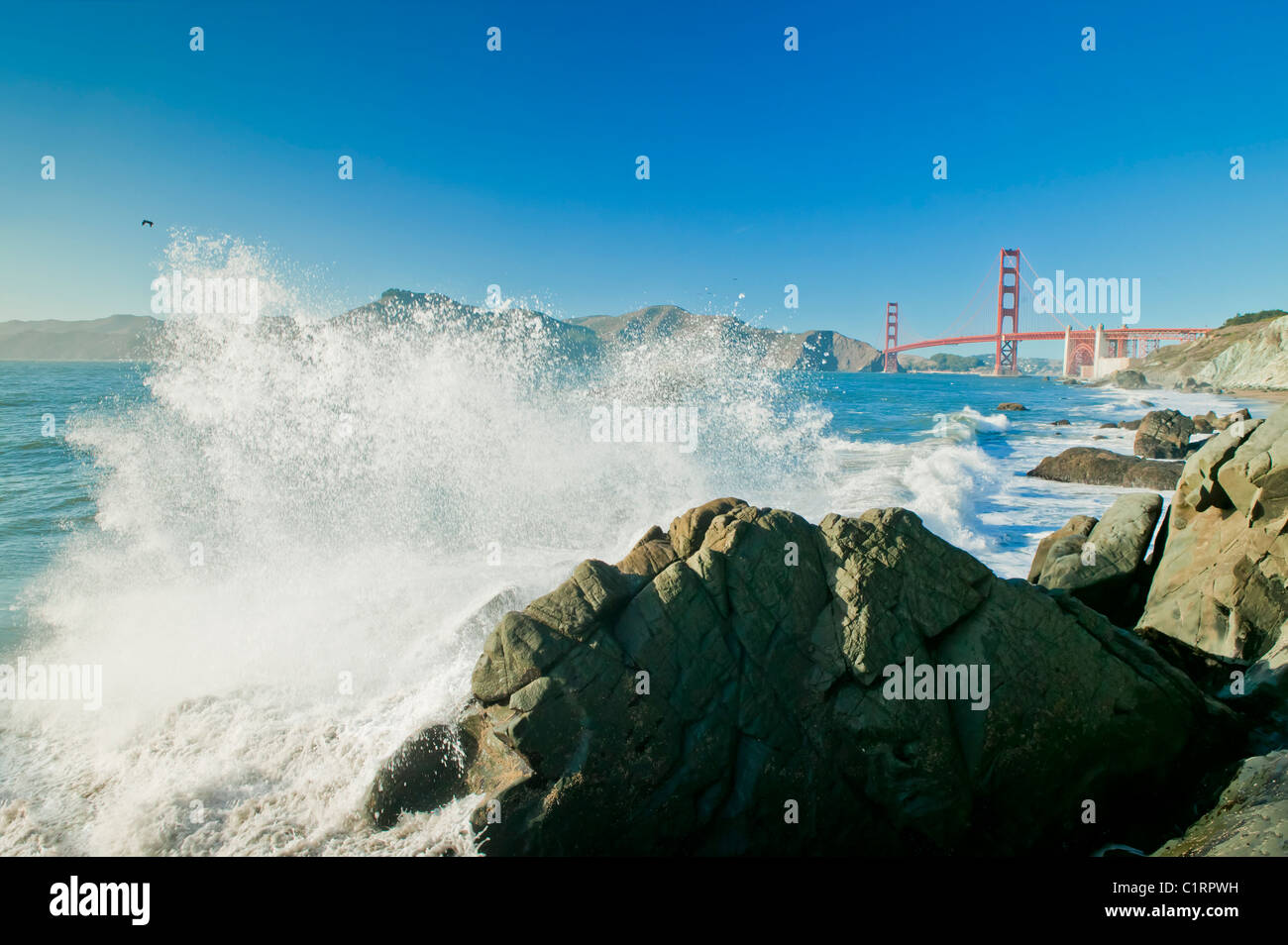 Eine große Ozeanwelle Absturz in Fels am Baker Beach, Golden Gate Bridge im Hintergrund Stockfoto