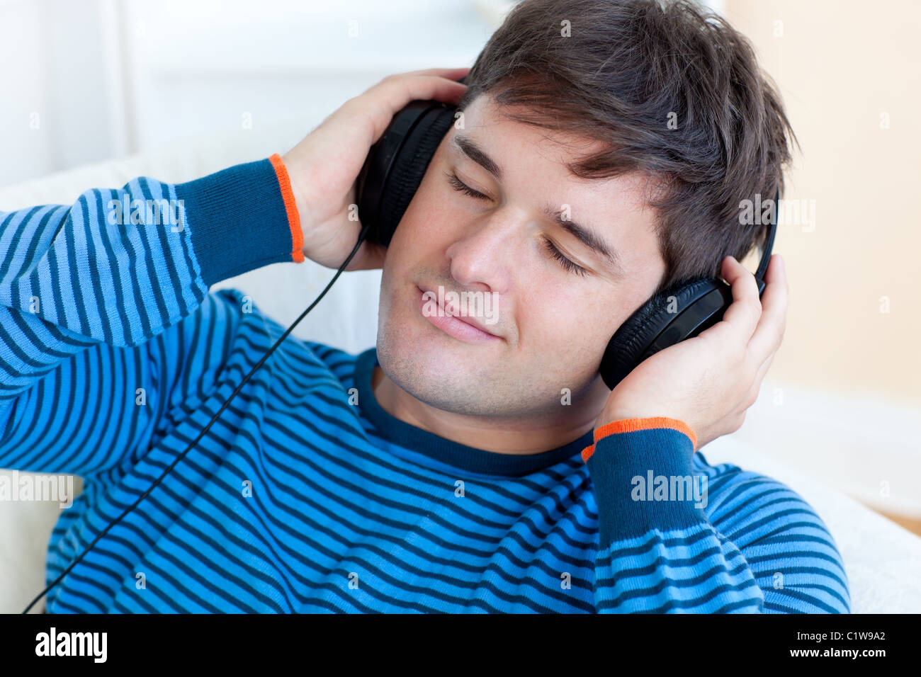 Friedliche Menschen hören Musik hält seine Kopfhörer auf dem sofa Stockfoto