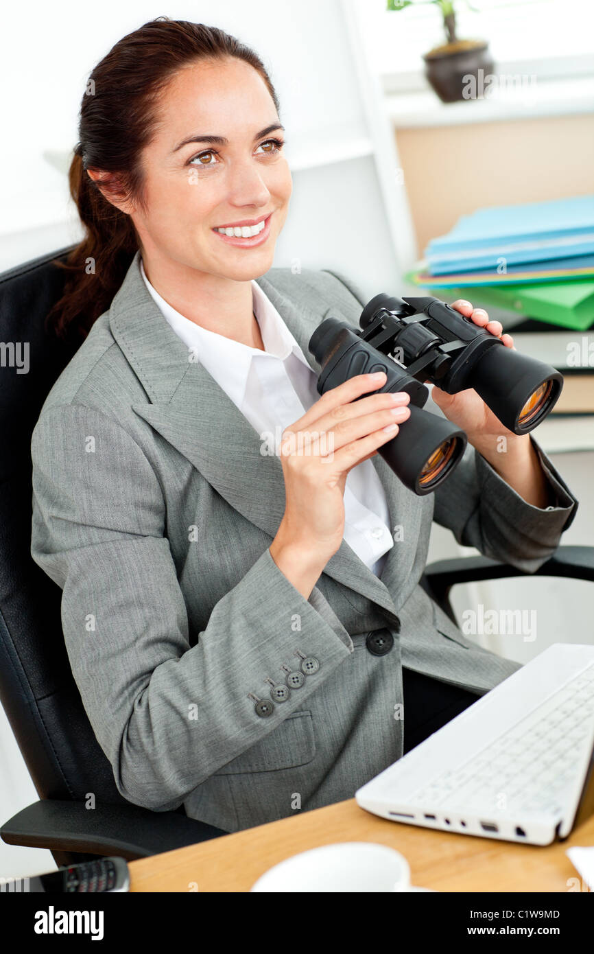 Strahlende Geschäftsfrau hält Fernglas sitzt an ihrem Schreibtisch Stockfoto