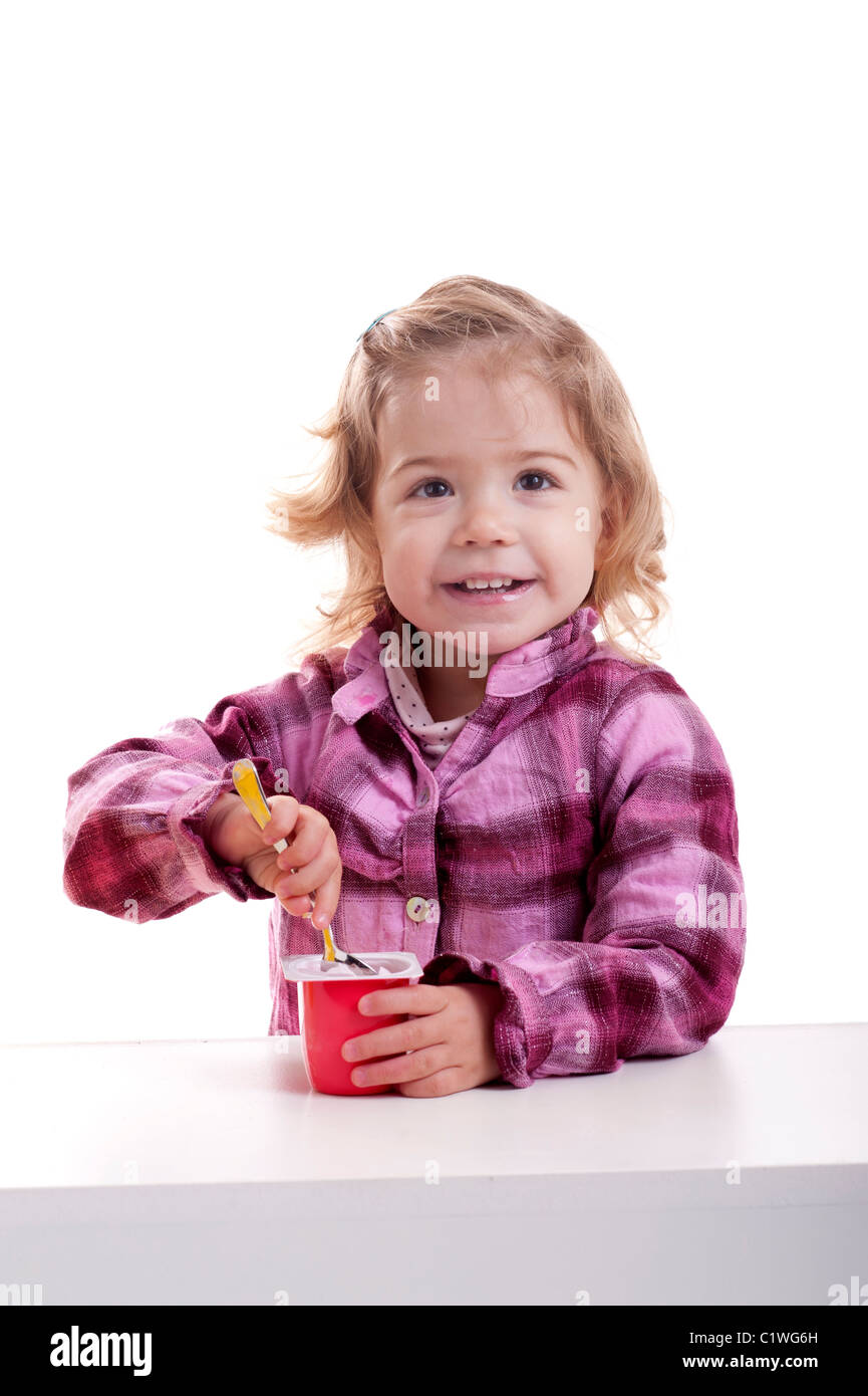 kleine Mädchen essen ein petit Suisse. isoliert auf weiss Stockfoto