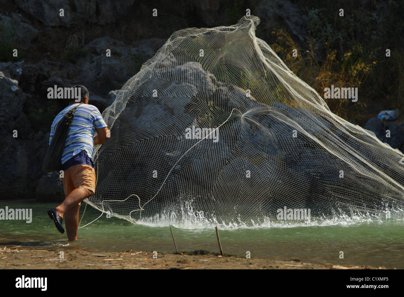 Mann ein Fischernetz im Fluss gegenüber den Felsen zu werfen. Sarigerme, Ägäis, Mittelmeer, Türkei Stockfoto