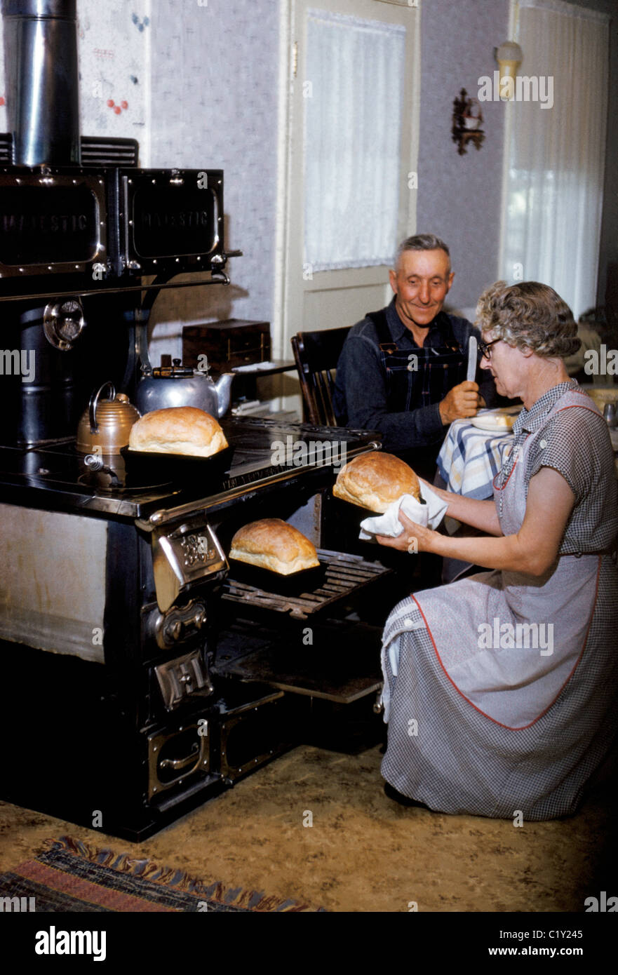 In den 1970er Jahren verwendet eine ältere Frau ihre Vintage Holz-brennenden Koch-Ofen zum Backen von Brot in der Küche ihr altes Bauernhaus in Tremonton, Utah, USA. Stockfoto