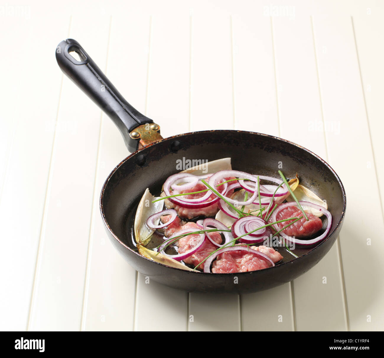 Rohes Schweinefleisch, Zwiebeln und Endiviensalat lässt auf einer Pfanne Stockfoto