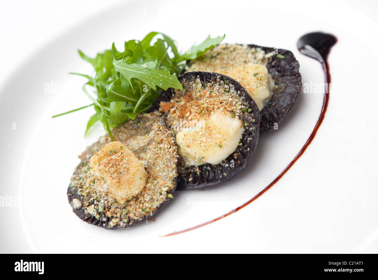 Starter der große flache Champignons gefüllt mit Paniermehl und Käse serviert mit Rucola und Balsamico-Dressing. Stockfoto