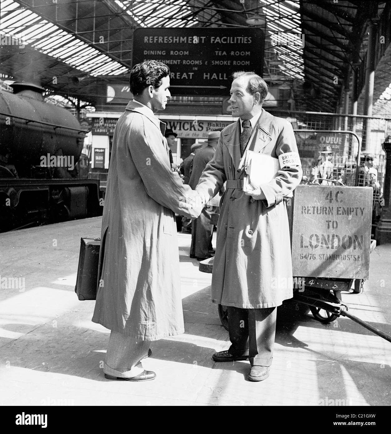 1950, historisch, begrüßt ein Beamter des British Council einen neu angekommenen männlichen Einwanderer auf einer Plattform am Bahnhof Euston, London, England. Stockfoto