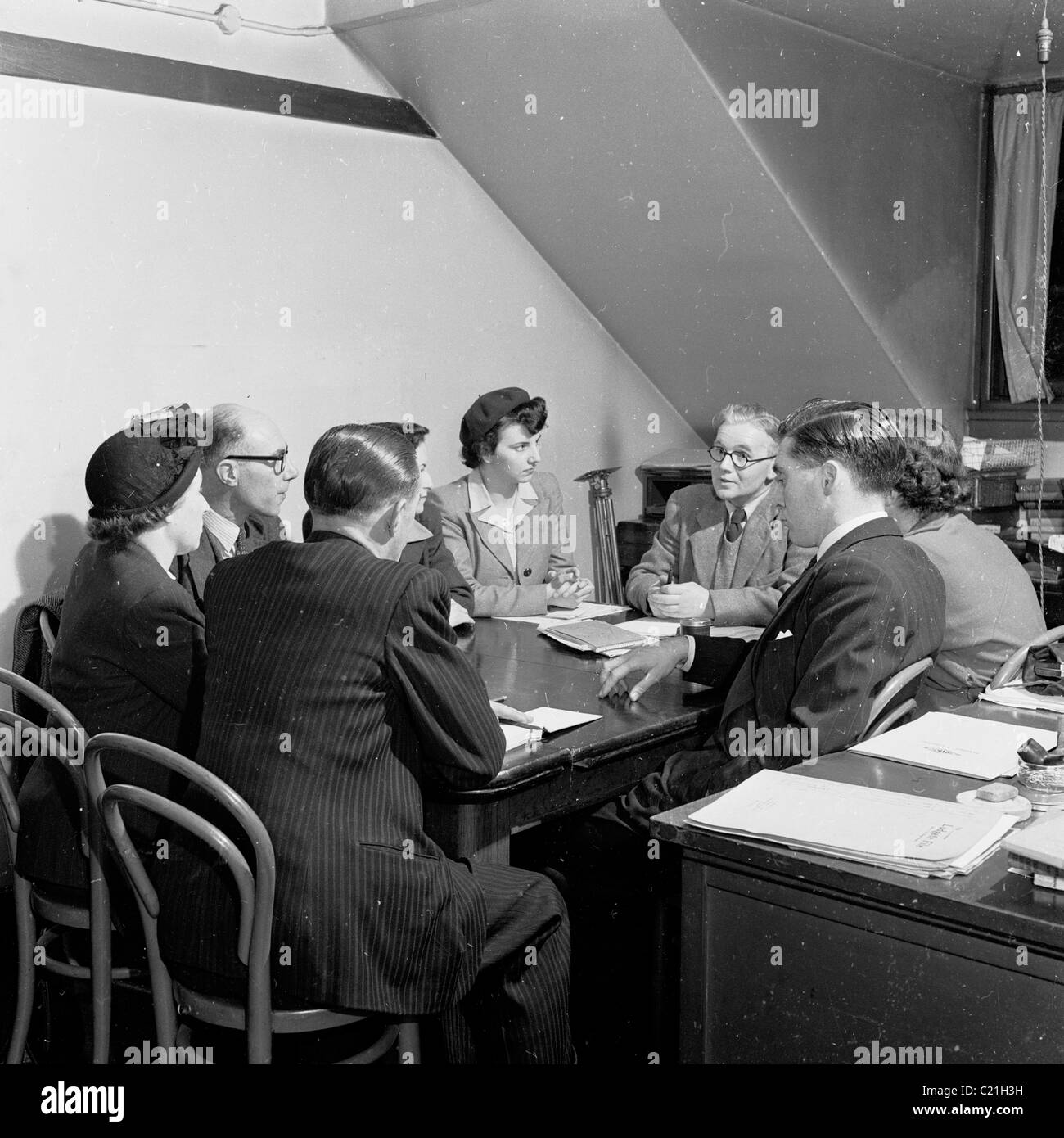 1950er Jahre, England. Kleine Gruppe von Männern und Frauen, die eine geschäftliche Konferenz, sitzen um einen Tisch in einem Manager in diesem historischen Bild. Stockfoto