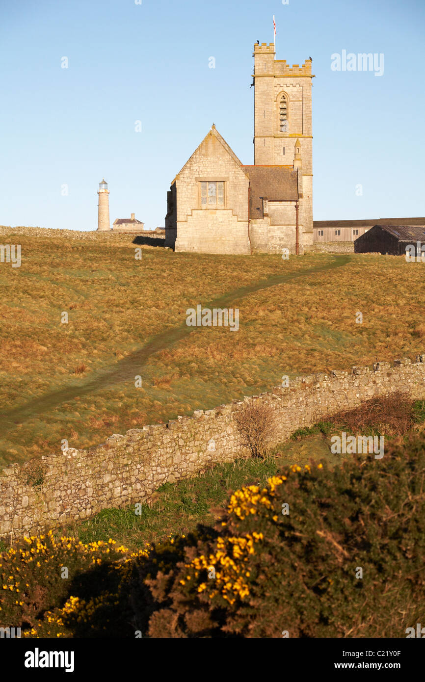St. Helena Kirche mit alten Leuchtturm Leuchtturm in der Ferne gebadet im Morgenlicht auf Lundy Island, Devon, England UK im März Stockfoto