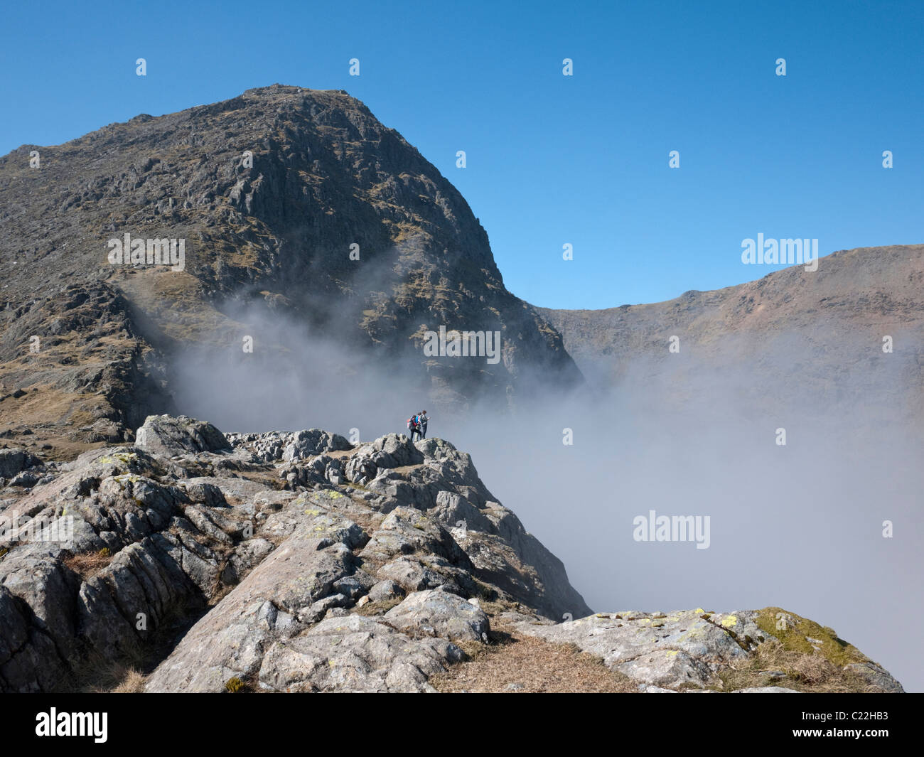 Wanderer bewundern eine Wolke Inversion in Cwm Dyli aus Bwlch y Saethau. Yr Wyddfa, der Gipfel des Snowdon überragt. Stockfoto