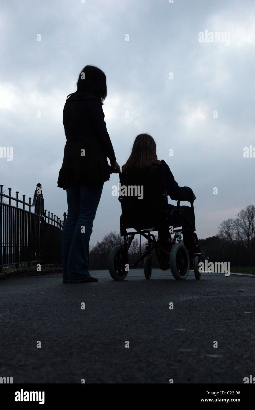 Junges Mädchen in einem Rollstuhl sitzt, mit einer Frau an ihrer Seite stehen Stockfoto
