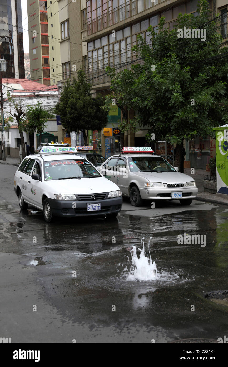 Taxis auf der Straße im Stadtzentrum und Wasserleck durch eine kaputte Leitung / Wasserleitung, Sopocachi, La Paz, Bolivien verursacht Stockfoto