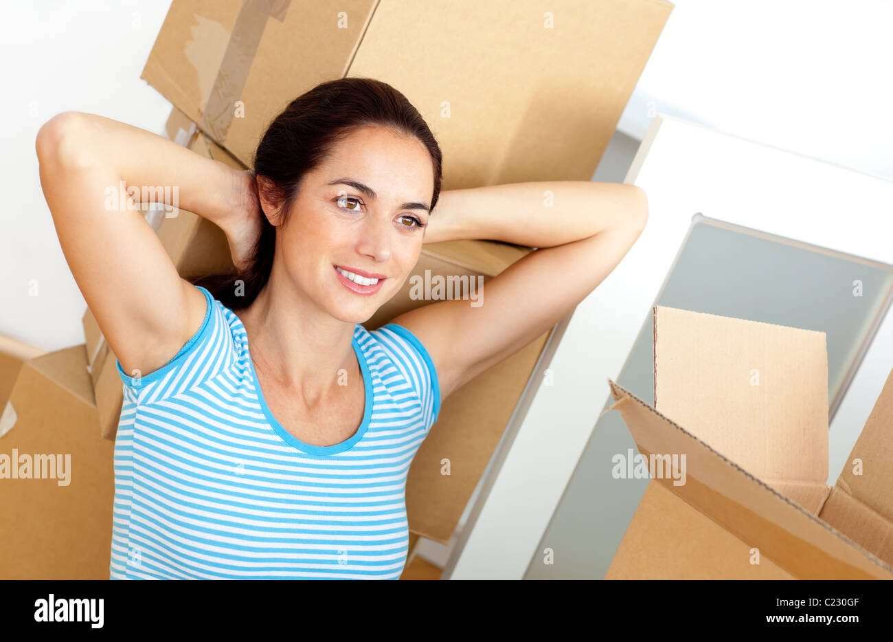 Entspannte junge Frau sitzt auf dem Boden nach dem Auspacken der Kartons Stockfoto