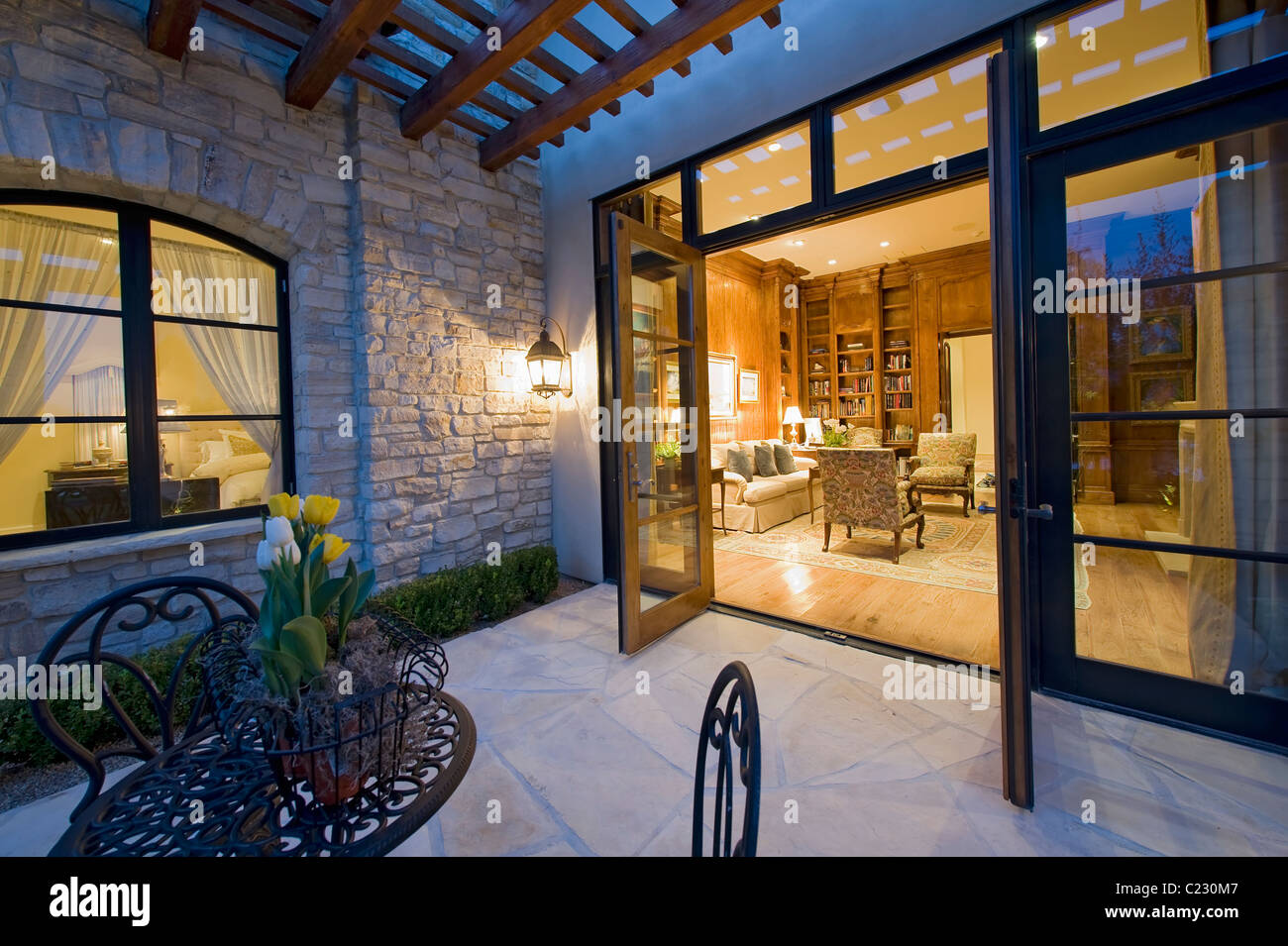 Haus außen in der Nacht mit einigen Patio-Möbel und offenen Terrassentüren, die auf der Suche in den beleuchteten Innenraum Stockfoto