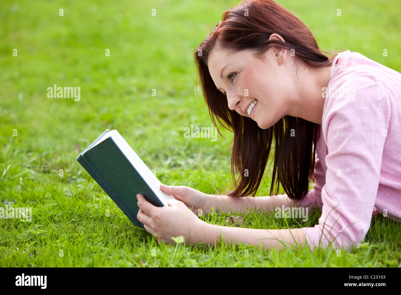 Nette junge Frau, die ein Buch auf dem Rasen liegen Stockfoto