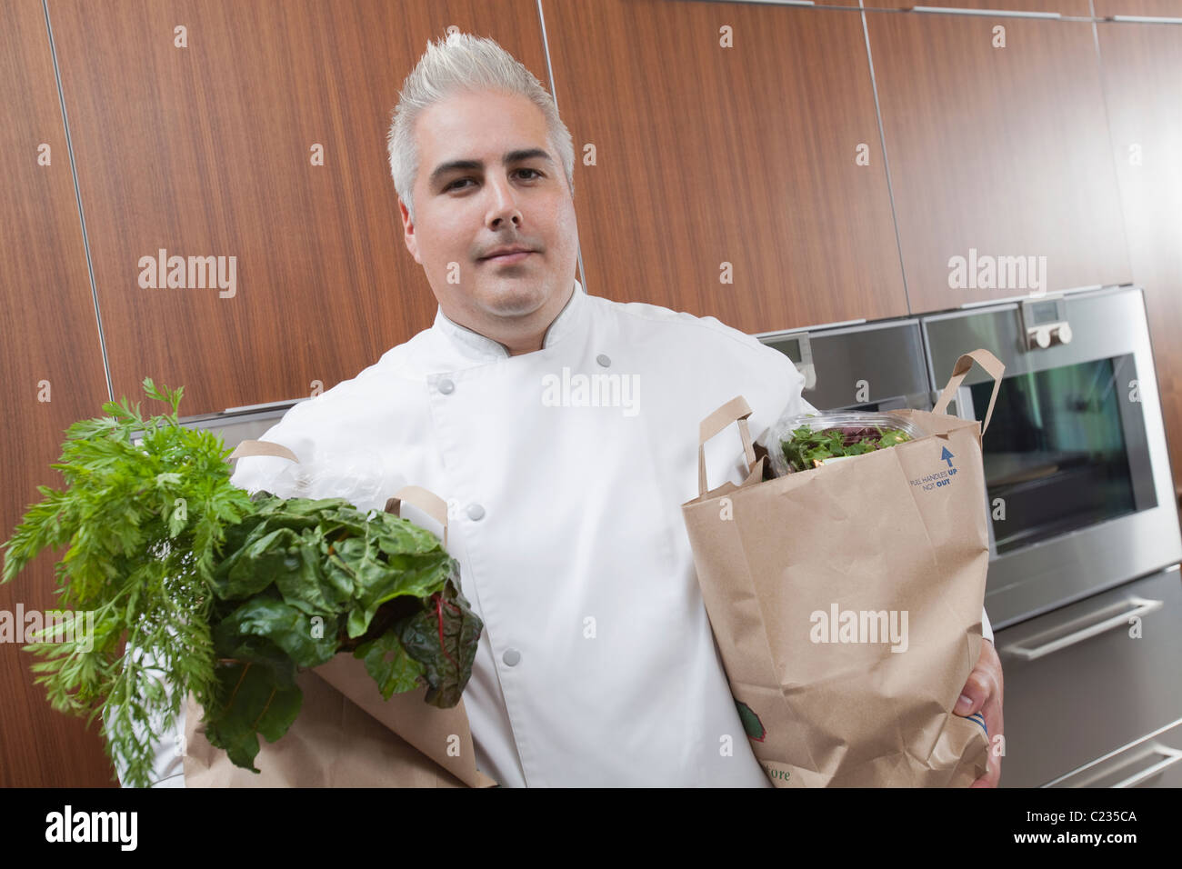 Mitte-Adult-Koch mit zwei Taschen von frischen Lebensmitteln Stockfoto