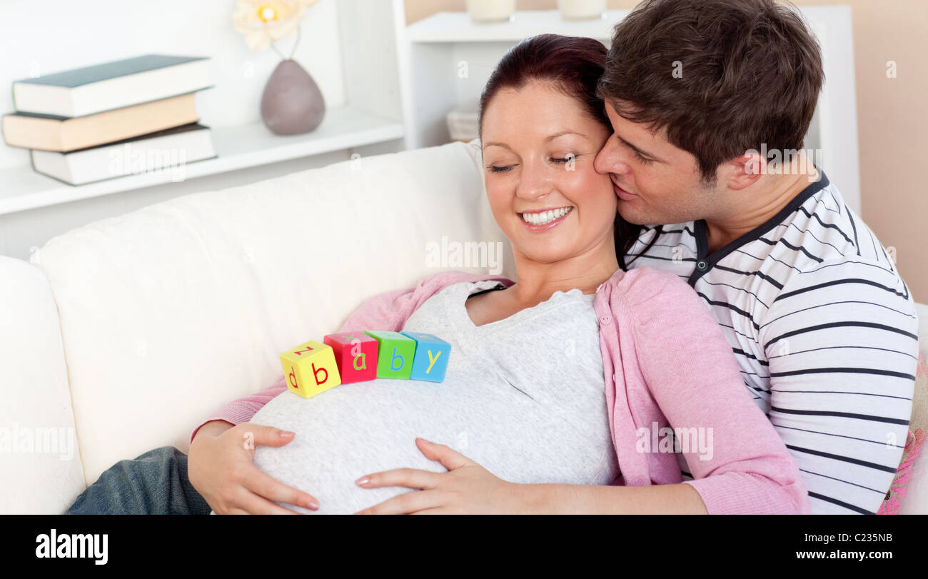 Junger Mann küssen seine schwangere Frau mit Baby auf dem Bauch liegend auf dem sofa Stockfoto
